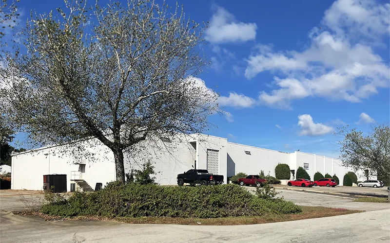 White building with parked cars and a tree under a blue sky with clouds