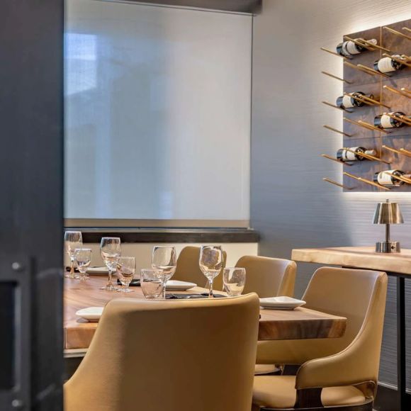 Dining area with wooden table, chairs, and wine glasses in a modern setting.