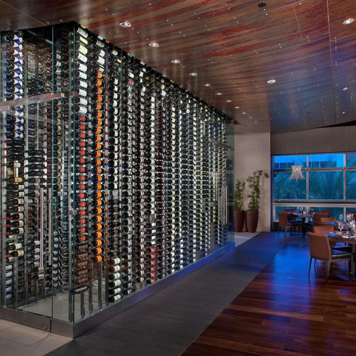 Wine rack with thousands of bottles in a modern room with wooden floor and large windows.