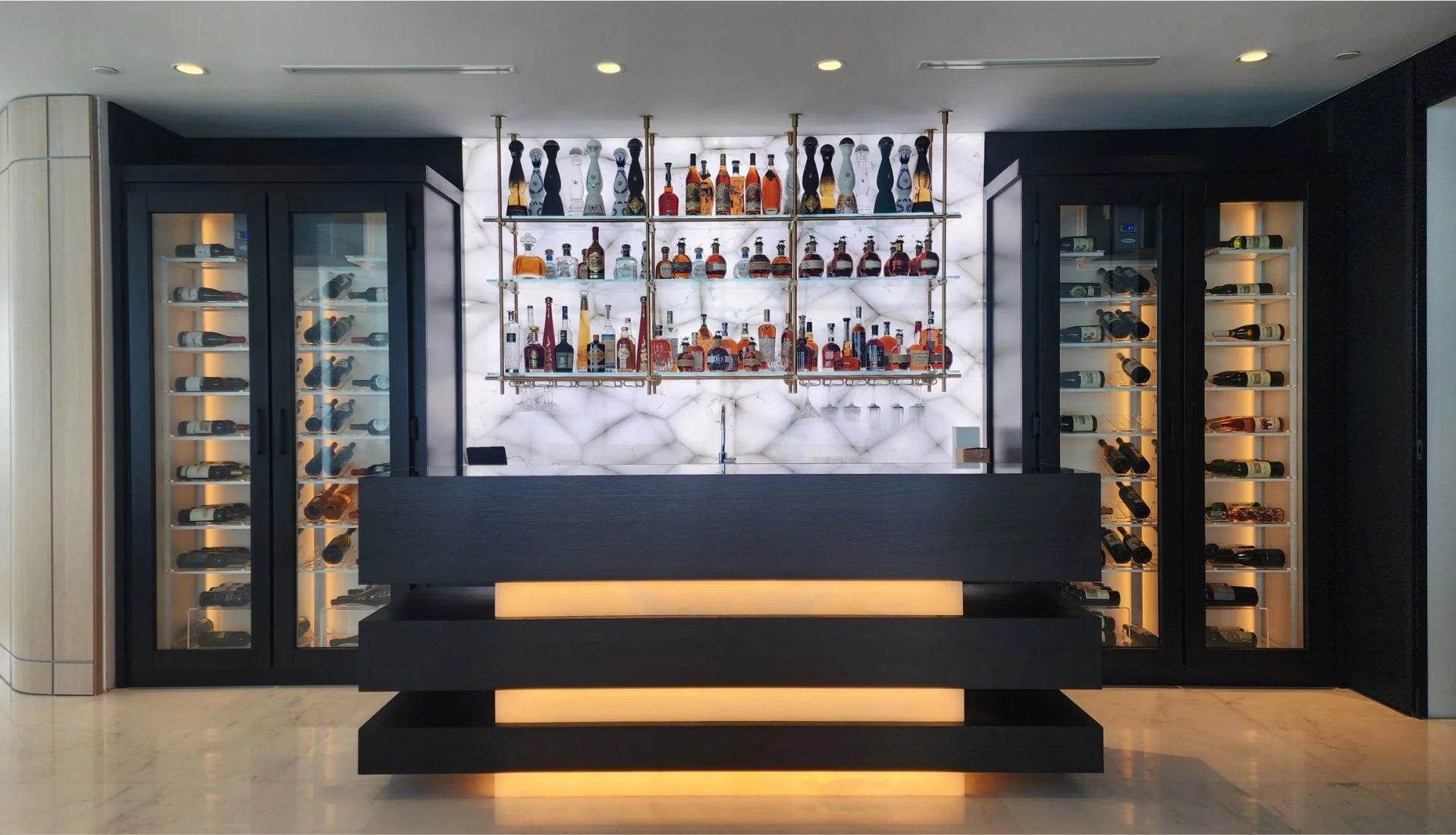 Modern conditioned wine cabinets with LED lighting flanking a backlit bar display in a luxury home.