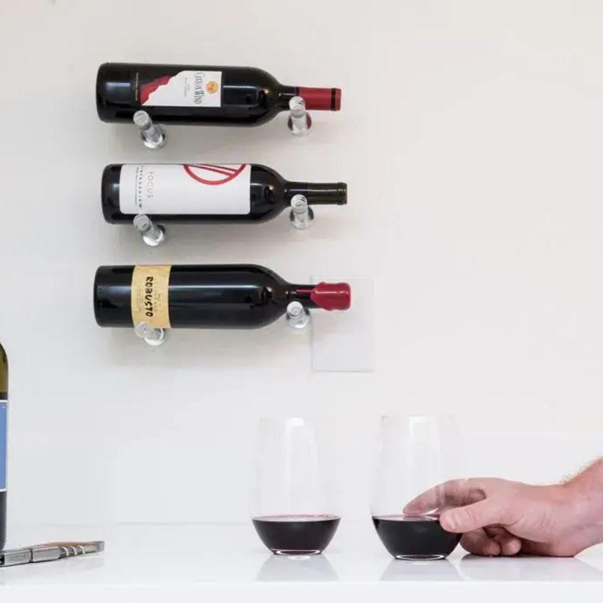 Clear acrylic wine pegs mounted on wall above counter with wine glasses for modern minimalist storage