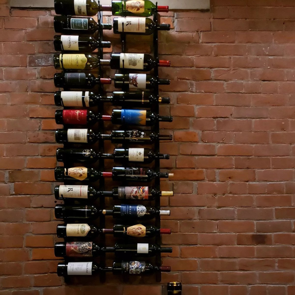 Wine bottles arranged on a wall-mounted rack against a brick wall.