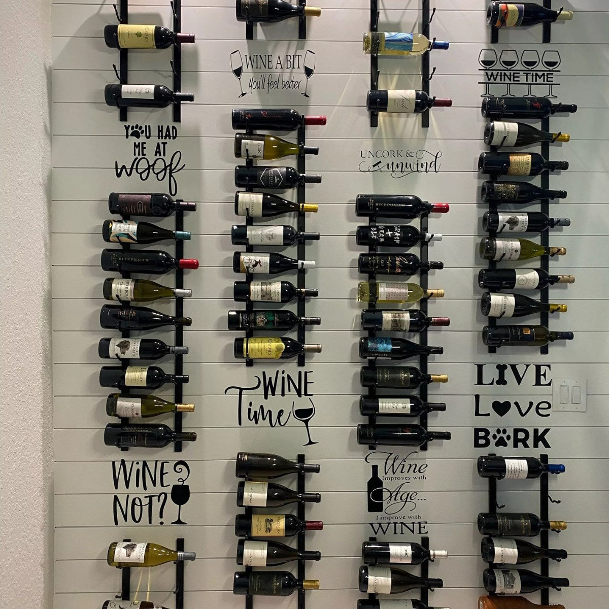 Wall-mounted wine rack with various wine bottles and decorative text labels.
