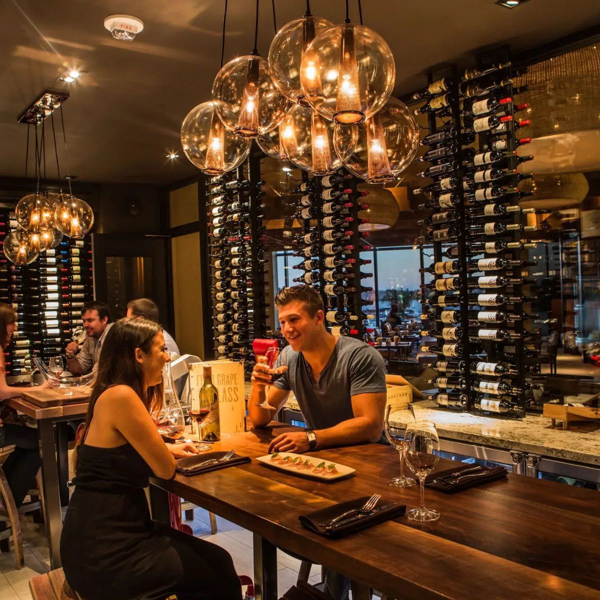 People dining at a restaurant with wine bottles and chandelier in the background